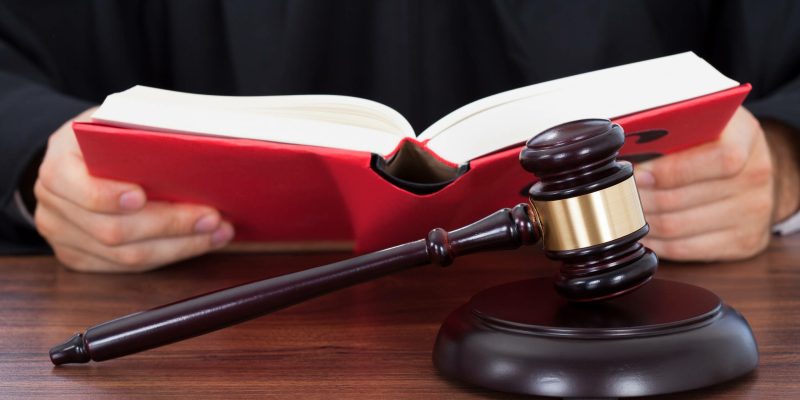 Closeup of gavel placed on block with judge reading law book at desk